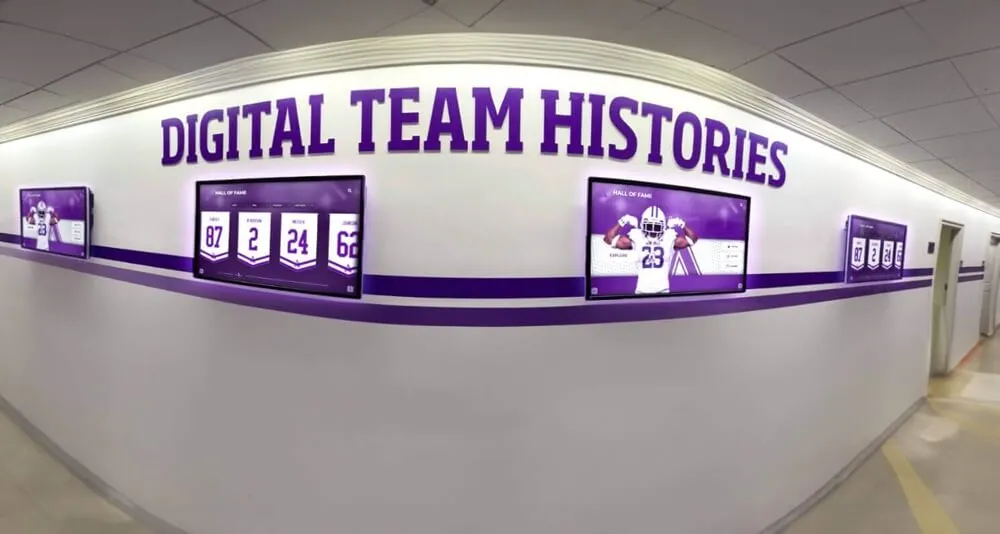 School hallway featuring digital team histories displayed on purple screens showing athletic recognition content Hallway with digital team histories displayed on purple screens