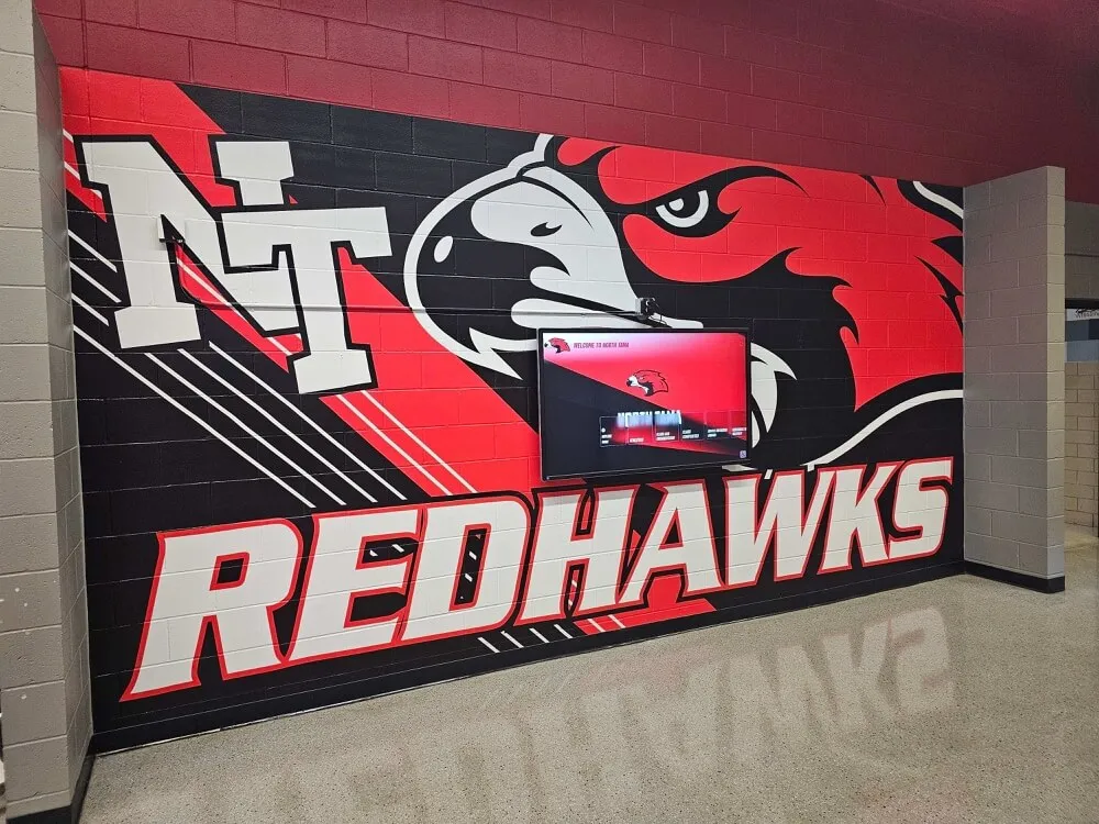 Redhawks school hallway mural with digital recognition screen — athletic award records displayed on screens like these originate from seasonal import workflows whose cluster-wide WAL activity is tracked in pg_stat_wal Redhawks mural in a school hallway with a TV screen showing digital recognition content beside colorful athletic mascot artwork